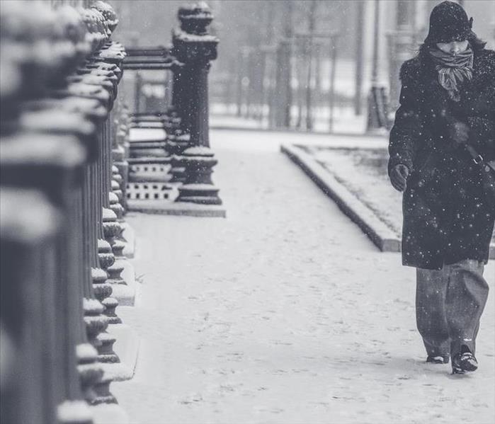 Woman bundled up walking in blizzard along a sidewalk in town.